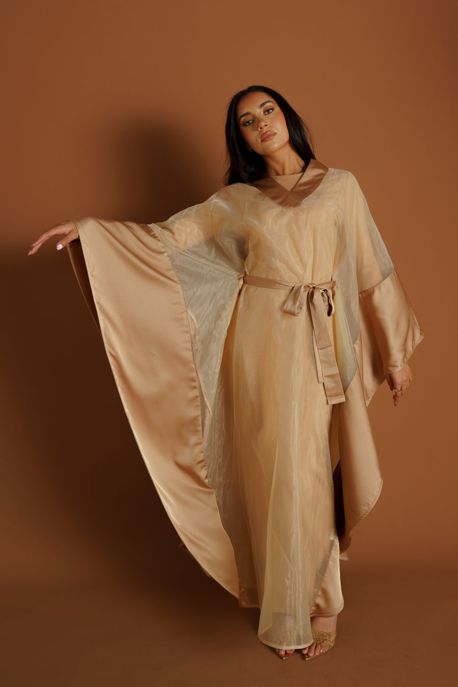 A model in the Saphire abaya set — champagne organza with a satin lining, sleeves opened wide.